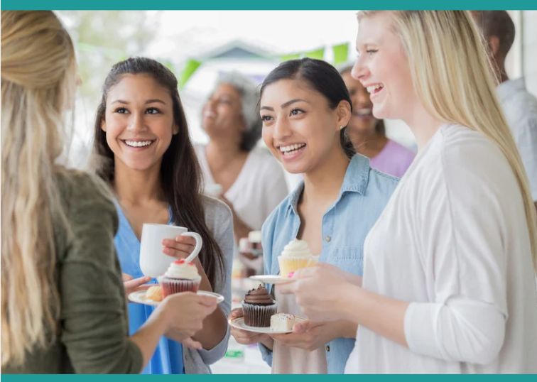 Group of women chatting and laughing while holding cakes and hot drinks in their hands